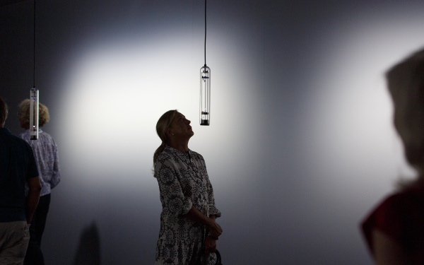 Das Bild zeigt eine Frau die auf eine Klanginstallation hochschaut die in längliches Glas gefasst ist